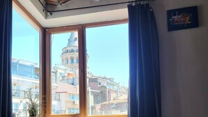 Ein Zimmer mit einer Couch, einem fensterbelaubten Fenster, einem Heizkörper und Blick auf Gebäude.