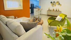 Ein modernes Wohnzimmer mit einer Couch, einem grünen Sessel und einem Essbereich im Hintergrund.