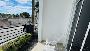 Ein Balkon mit zwei weißen Stühlen, einer Glastür und einer Steinmauer mit Grünpflanzen.