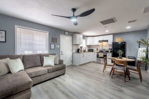 A modern living room with a sofa, dining table, and kitchen in the background. - 1BR/1BA Chic Home • King Bed • Smart TV’s (El Paso)