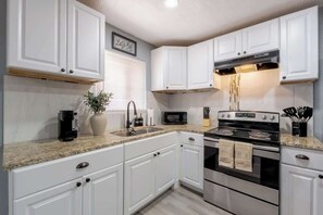 A kitchen with white cabinets, a granite countertop, a stove, a microwave, and a sink. - 1BR/1BA Chic Home • King Bed • Smart TV’s (El Paso)
