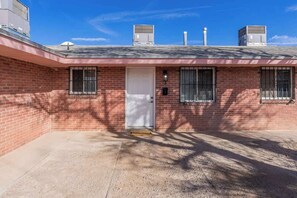 A two-story brick building with a white door, two windows with metal bars, and two air conditioning units on the roof. - 1BR/1BA Chic Home • King Bed • Smart TV’s (El Paso)