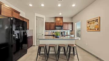 A modern kitchen with a black refrigerator, wooden cabinets, a central island with stools, and a decorative painting on the wall.