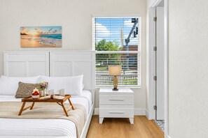Un dormitorio con cama, mesita de noche, lámpara y un cuadro de una playa.