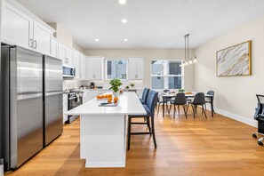 A modern kitchen with white cabinets, a stainless steel refrigerator, and a central island with seating. - Ultimate Tampa Stay | Dual Units • 6BR • Sleeps 17 (Tampa)