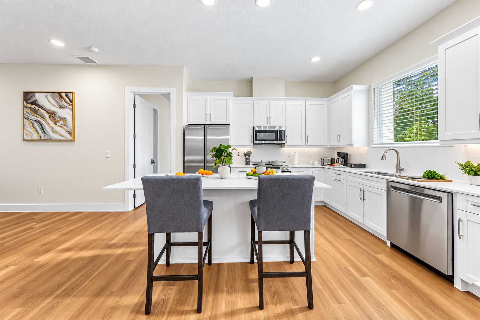 A modern kitchen with white cabinets, stainless steel appliances, and a wooden floor.
