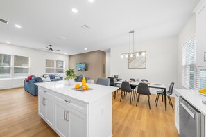 A modern kitchen with white cabinetry, a central island, and a dining area with a table and chairs. - Ultimate Tampa Stay | Dual Units • 6BR • Sleeps 17 (Tampa)