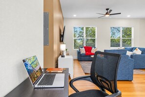 A modern living room with a laptop on a desk, a blue sofa, and a ceiling fan. - Ultimate Tampa Stay | Dual Units • 6BR • Sleeps 17 (Tampa)