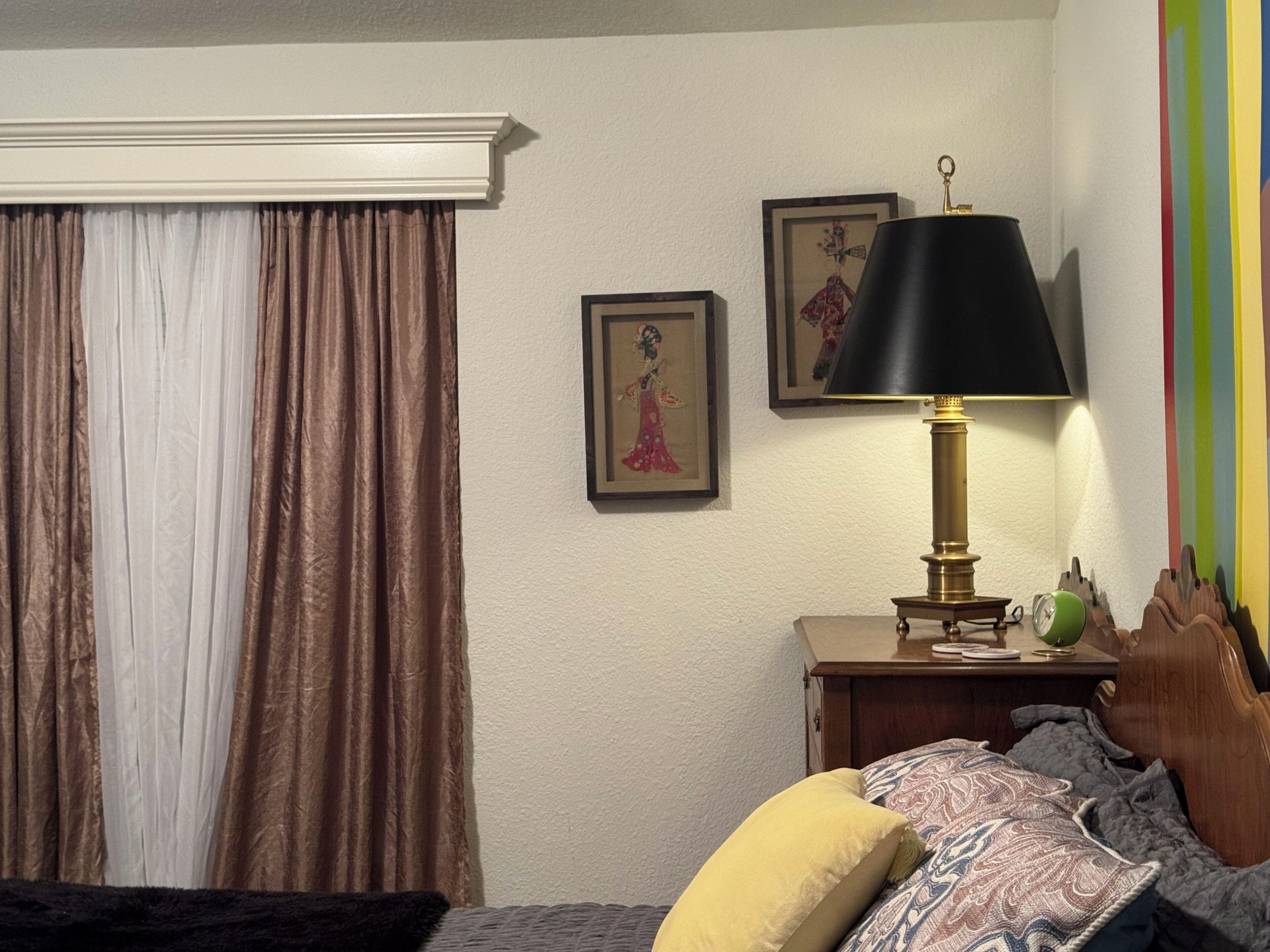 Ein Schlafzimmer mit einem Bett, einem Nachttisch mit Lampe, einem gerahmten Bild und einem Fenster mit Vorhängen.