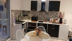 A modern kitchen with a black stove, white chairs, a small dining table, and a decorative chandelier.