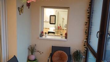 A small, cozy room with two chairs, a table, a hanging light fixture, a window with a mirror, and a potted plant.
