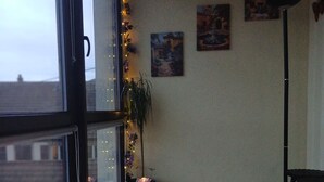 A room with a large window, a potted plant, a floor lamp, a small table with a lamp, and a chair.
