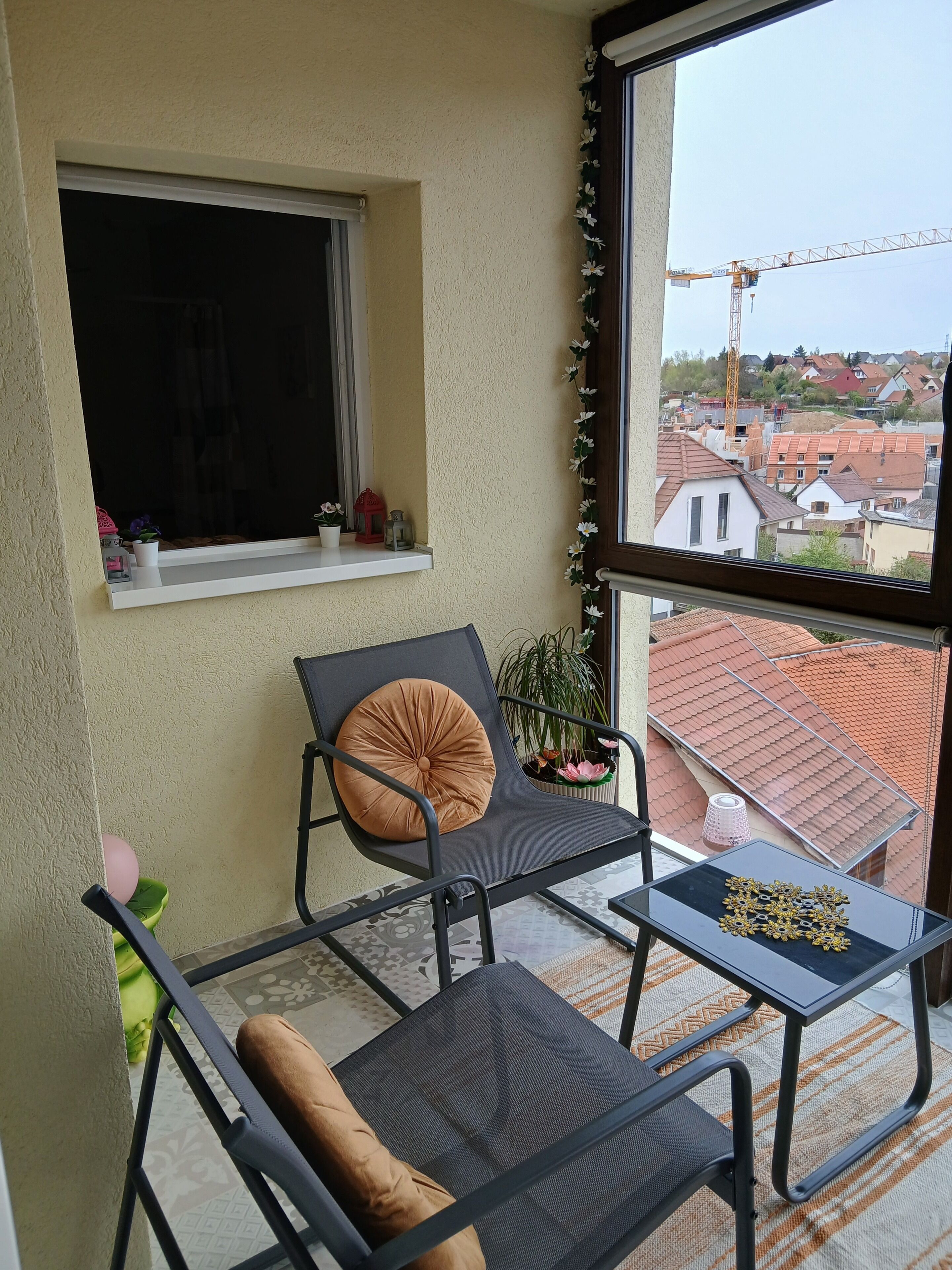Un balcon avec une chaise, une petite table et une fenêtre donnant sur un quartier résidentiel.