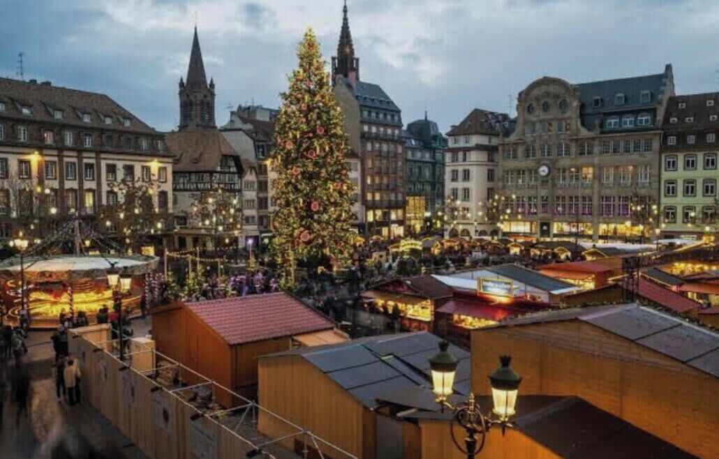 Een historisch stadsplein met een opvallende kerstboom, traditionele gebouwen en een markt.