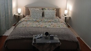 A bedroom with a bed, two bedside lamps, a small table with a decorative item, and a hanging light fixture.