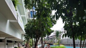 A pathway leading to a pool area with a modern building in the background. - Cozy gated studio apartment in Central Jakarta with AC, fitness room, and pool (Jakarta Pusat)