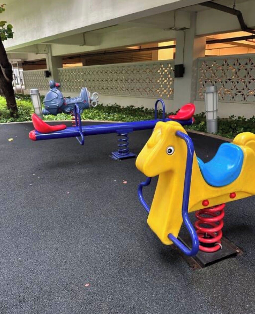 Outdoor playground equipment, including seesaws and a horse-shaped ride, under a covered area.