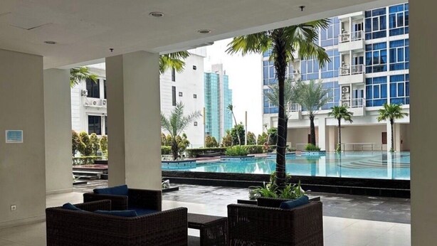 A spacious indoor area with a pool, wicker furniture, and a view of high-rise buildings. - Cozy gated studio apartment in Central Jakarta with AC, fitness room, and pool (Jakarta Pusat)