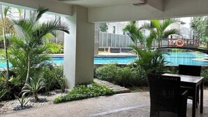 An outdoor patio area with a pool view, covered seating, and greenery. - Cozy gated studio apartment in Central Jakarta with AC, fitness room, and pool (Jakarta Pusat)