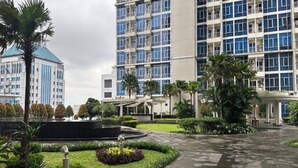 A hotel with a modern design, featuring a central courtyard with a fountain, surrounded by well-maintained greenery and palm trees. - Cozy gated studio apartment in Central Jakarta with AC, fitness room, and pool (Jakarta Pusat)