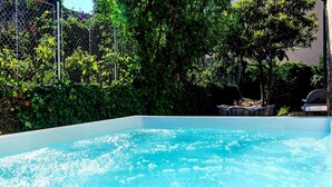 Una piscina con superficie de agua azul cristalina, rodeada de exuberante vegetación y una cerca de metal.