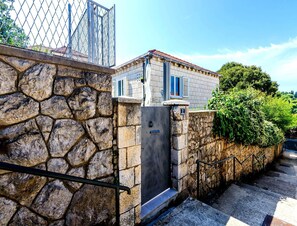 A stone wall with a metal gate, a metal door with a number plate, and a staircase leading to a building with a tiled roof. - Rustic Stone Villa With Private Pool & Garden (Solin)