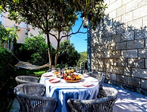 An outdoor dining area with wicker chairs and a table set for a meal, surrounded by greenery and a stone wall. - Rustic Stone Villa With Private Pool & Garden (Solin)
