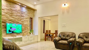 Ein Wohnzimmer mit Steinwand, Flachbildfernseher, Ledersofas, Esstisch mit Stühlen und einer Deckenleuchte.