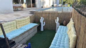 Ein Poolbereich mit integriertem Sitzbereich, einer Kakteendekoration und einem Bambuszaun.