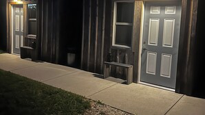 Un edificio de dos pisos con puerta principal y ventana en la planta baja, un pequeño porche y un camino que lleva a la puerta.