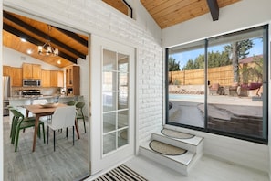 Eine moderne Küche mit Holzausstattung, ein Essbereich mit grünen Stühlen und eine große Schiebeglastür, die auf eine Außenpatio mit Pool und Gartenmöbeln führt.