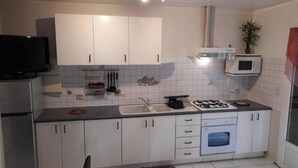 A kitchen with white cabinets, a microwave, a gas stove, and a refrigerator. - T2 furnished with terrace and pool - Saint-Louis 🌺. 🌴 (Saint-Louis)