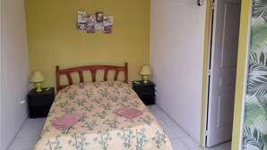 A bedroom with a bed, two bedside tables, a wall-mounted fan, and a door. - T2 furnished with terrace and pool - Saint-Louis 🌺. 🌴 (Saint-Louis)