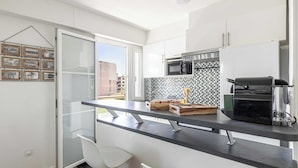 Een moderne keuken met een zwart aanrecht, witte kastjes, een magnetron, een koffieapparaat en uitzicht op buiten.