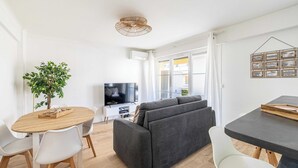 Een moderne woonkamer met een bank, eettafel, stoelen, een televisie en een plant.