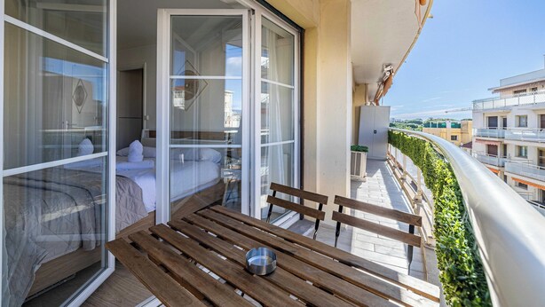 Een balkon met een houten tafel, een metalen schaal en een bed met wit beddengoed.