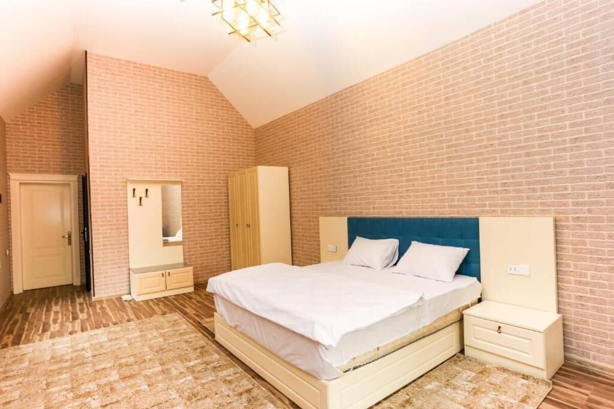Un dormitorio con pared de ladrillo, cama con ropa de cama blanca, mesita de noche, armario y espejo.