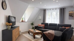 Een moderne woonkamer met een bank, een salontafel, een tv op een meubelstuk en een raam met gordijnen.