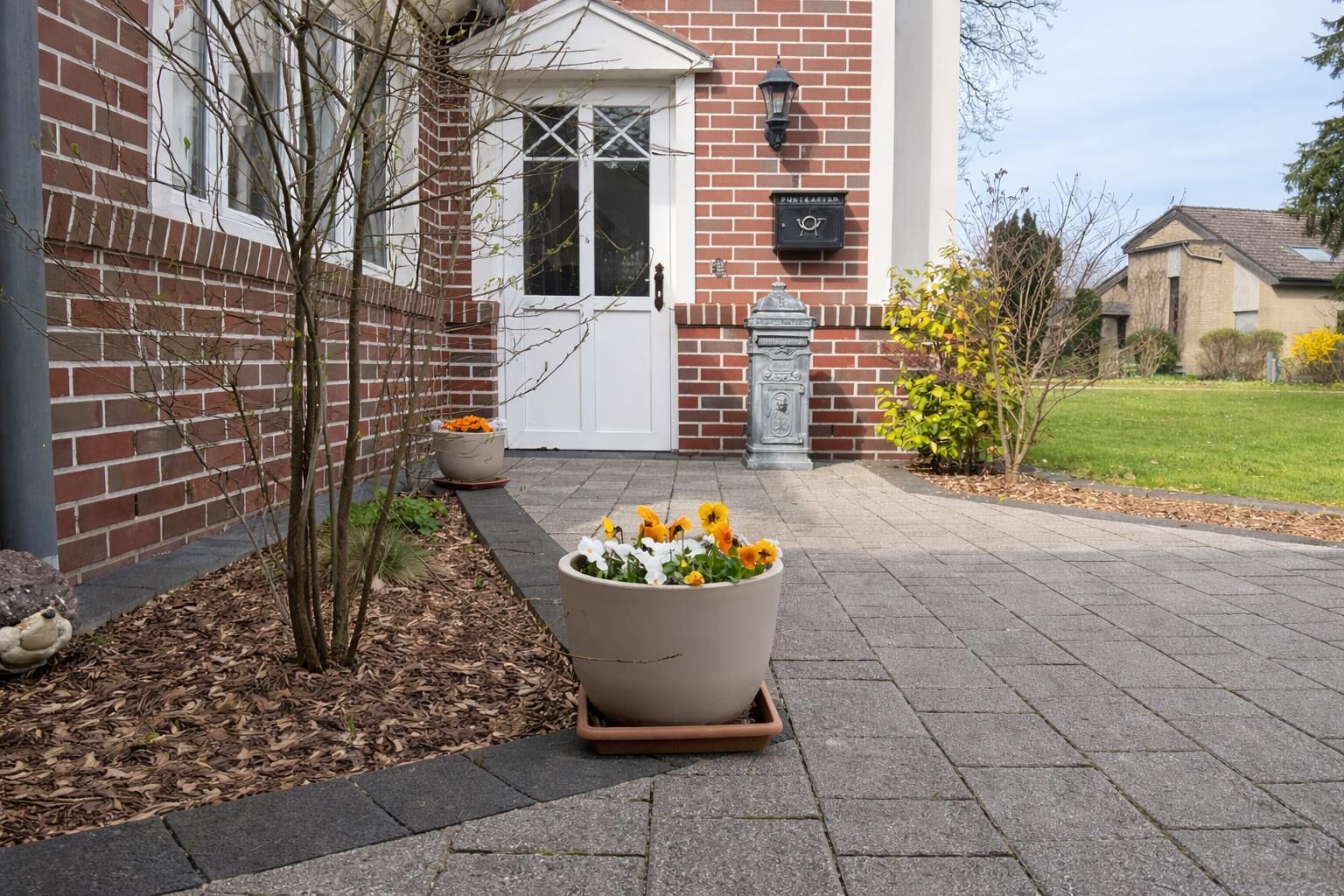 A brick building with a white door, a flower planter in front, and a well-maintained lawn.
