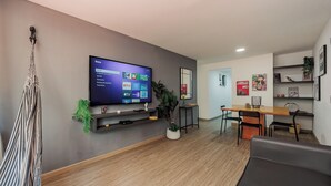 A modern living room with a flat-screen TV, a hammock, a dining area with a table and chairs, and a wall with framed pictures and a plant. - Perfect 3-bedroom apartment in Medellín for a relaxing stay (Medellín)