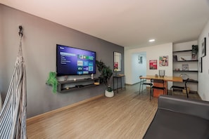 A modern living room with a flat-screen TV, a hammock, a dining area with a table and chairs, and a wall with framed pictures and a plant. - Perfect 3-bedroom apartment in Medellín for a relaxing stay (Medellín)