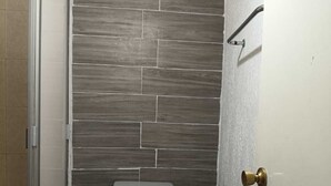 Een badkamer met een toilet, een prullenbak en een douche.