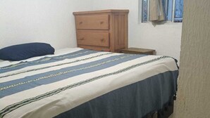 Een slaapkamer met een bed, een houten dressoir en een raam met gordijnen.