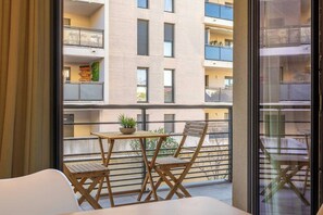 A balcony with a table and chair, a potted plant, and a view of a multi-story building. - Spacious Studio a/c 2P - Place des Lices (Saint-Tropez)