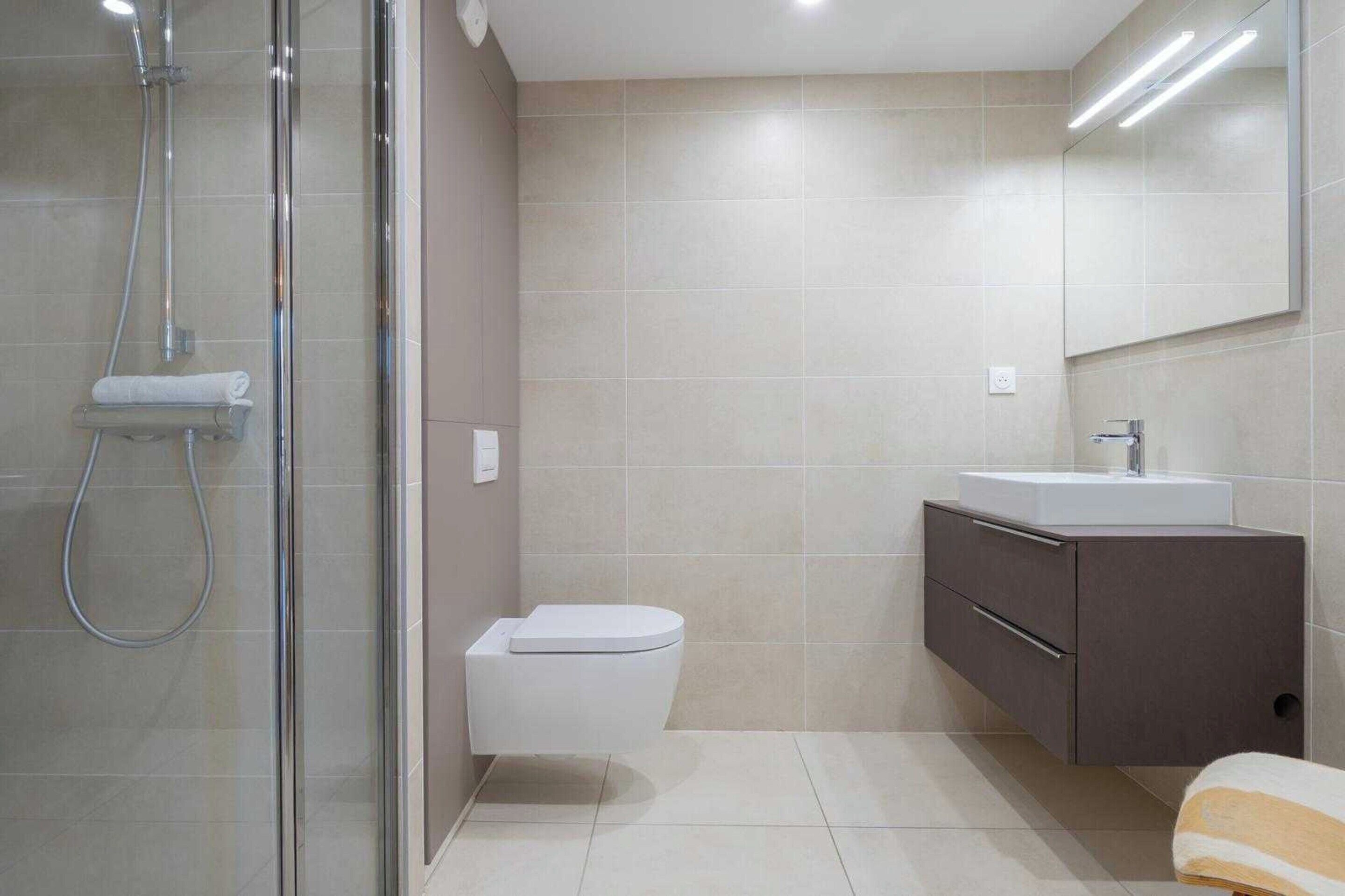A modern bathroom with a glass shower enclosure, a toilet, a sink, and a cabinet.