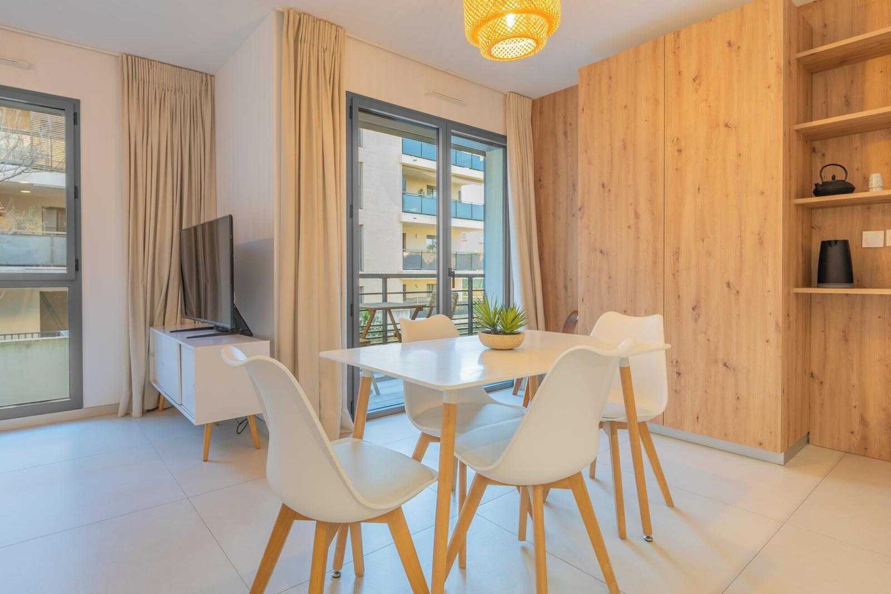 A modern living room with a dining table, white chairs, a TV, and a wooden wall.