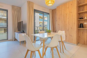 A modern living room with a dining table, white chairs, a TV, and a wooden wall. - Spacious Studio a/c 2P - Place des Lices (Saint-Tropez)