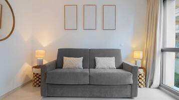 Um sofá cinzento com duas almofadas, duas luminárias de mesa e três quadros na parede.