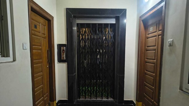 Un corridoio con un cancello in metallo nero, porte in legno e un interruttore sulla parete.