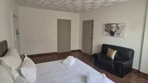 Habitación de hotel con una cama grande, un sofá de cuero negro, un cuadro en la pared e iluminación empotrada en el techo.